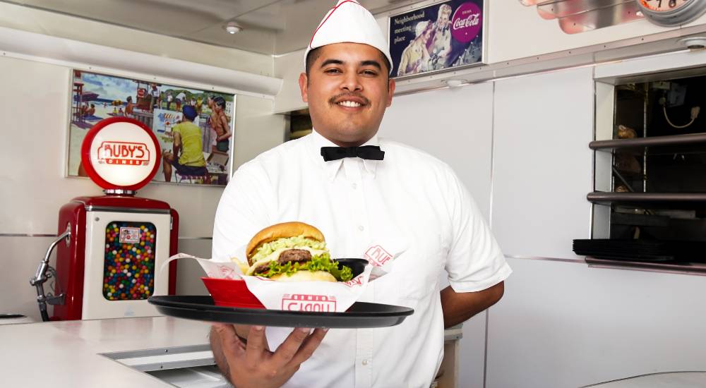 A smiling Ruby's waiter with a meal on a tray