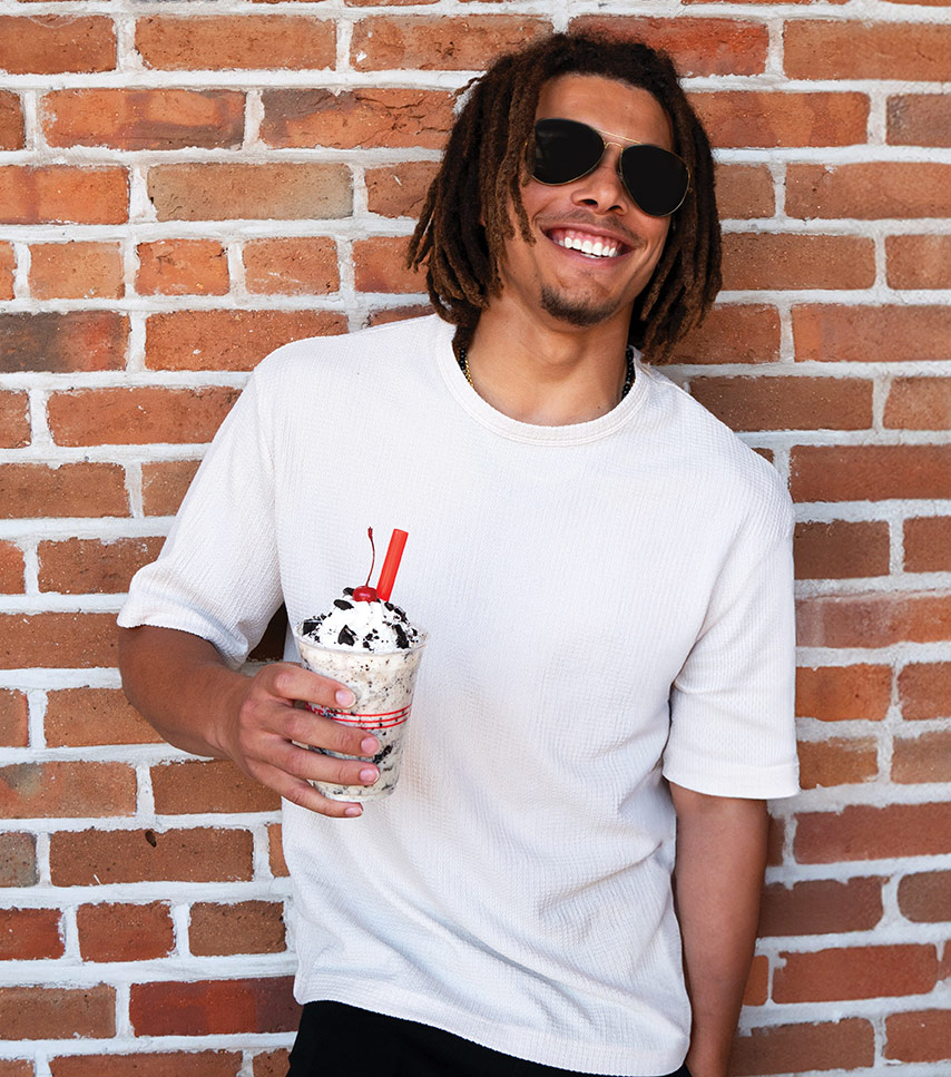 Guy leaning against a brick wall holding a Ruby's shake